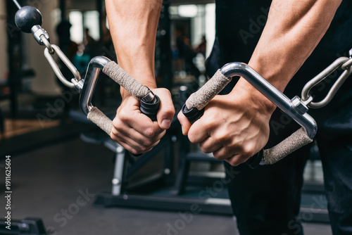 Strong male hands holding cable machine handles during workout in a gym.