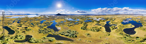 Aerial view of the vivid green and gold landscape dotted with dark, reflective pools near Lake Myvatn under a crisp blue sky, in 360 degrees panorama, Myvatn, Nordurland Eystra, Iceland.