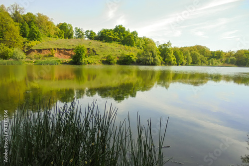 Feel the spring warmth near a pond surrounded by trees. Beautiful hilly landscape. Ukraine, Kharkiv region.