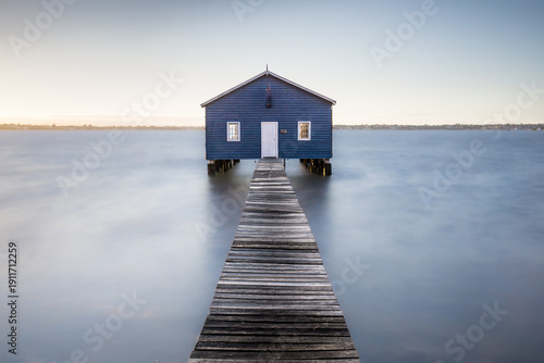 View of the iconic blue boat house stands serenely on stilts, connected by a weathered wooden jetty that stretches into the tranquil water, Perth, Western Australia, Australia.
