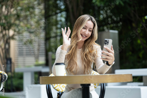 Photography A cheerful woman waves at her phone, embodying warmth and friendliness during an outdoor interaction