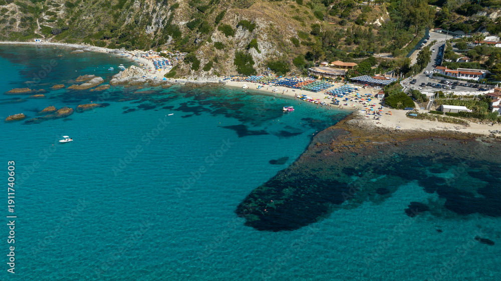 Obraz premium Aerial view Grotticelle beach, in Calabria, Southern Italy. Panorama of the Calabrian coast featuring a beautiful beach, lush green hills, vibrant turquoise waters, and submerged rocky reefs.