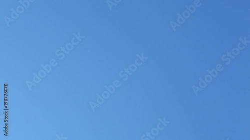 Soap bubbles drift across a clear blue sky in sunlight. Several bubbles enter from the left, rise and slide right with light wind, then fade as the last bubble exits frame.