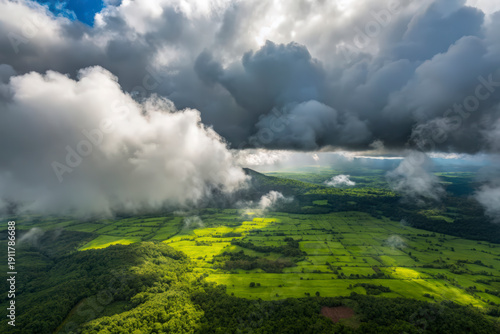 Stunning aerial panorama of vibrant green fields and dense forests bathed in sunlight under dramatic stormy clouds