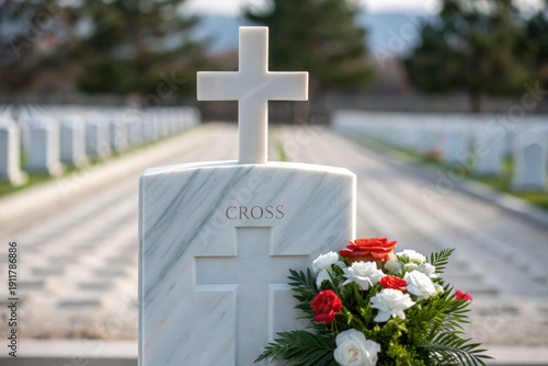 White marble cross tombstone adorned with red and white flowers at a solemn military cemetery
