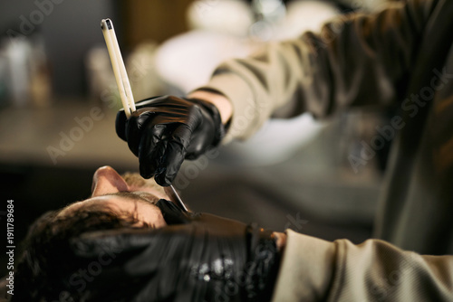 Fotografía Caucasian young adult man receiving professional shave from gloved barber using