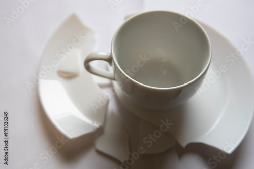 Broken cup and plate pieces on a white surface after an accident during breakfast in a kitchen
