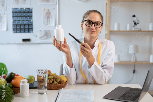 Portrait of woman nutritionist doctor demonstrating pills bottle at camera in office. food expert proposing dietary supplements