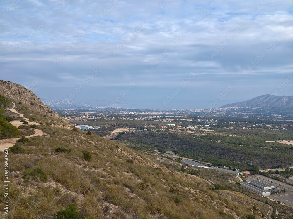 Fototapeta premium Charming hiking path through rocky terrain offering breathtaking views of nature and nearby urban backdrop