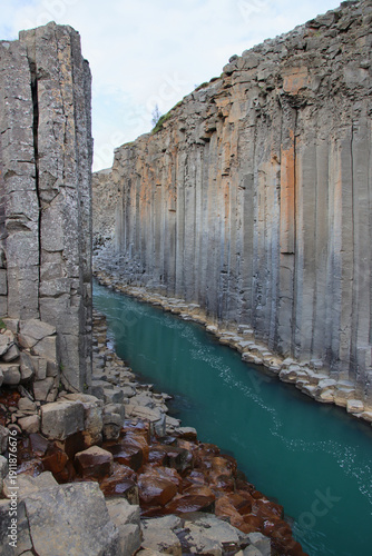 Turquoise glacial river flowing between vertical basalt columns in Stuðlagil Canyon, Jökuldalur valley, East Iceland, under soft daylight.