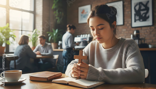 Asian girl teenager praying to God, holds christian cross in hands in cafe.