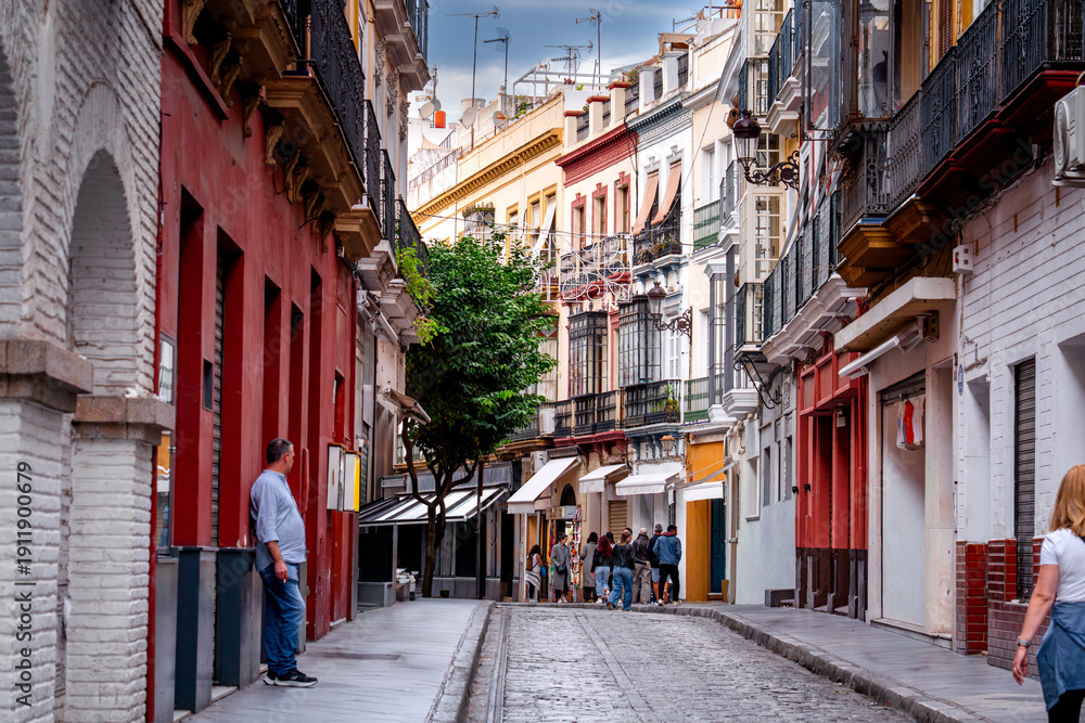 Fototapeta premium Narrow street in Seville with people, cafes, and restaurants, Spain, everyday life on streets Andalusia.