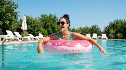 Happy Woman in Sunglasses Floating on Pink Donut Inflatable in Sunny Swimming Pool, Enjoying Summer Vacation and Refreshing Water
