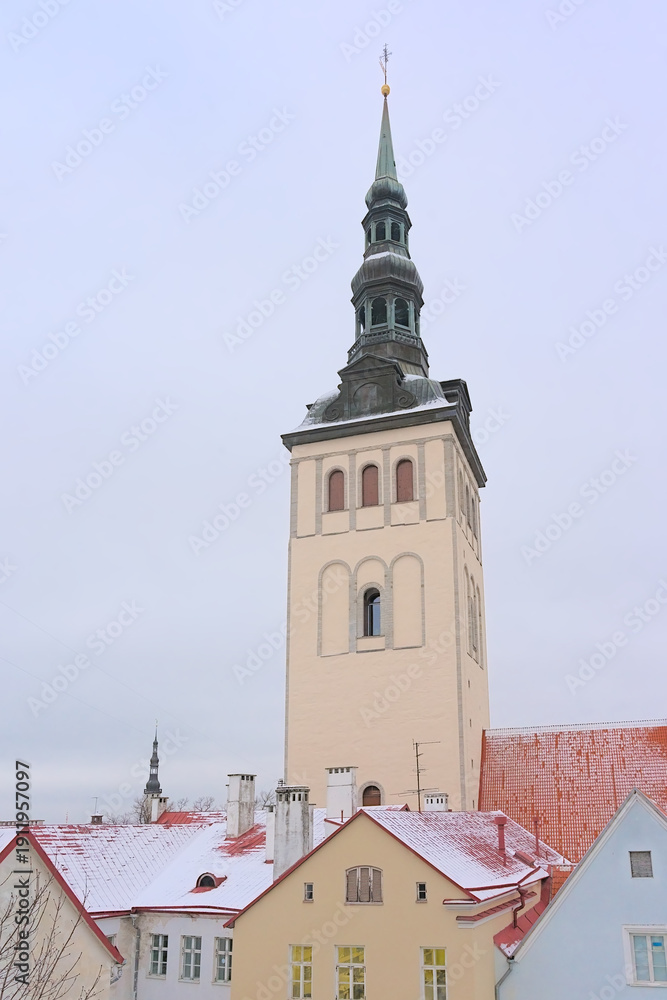 Obraz premium Clock tower of Saint Nicholas church over the snow covered roofs of medieval houses on a cold winter evening in Tallinn, Estonia