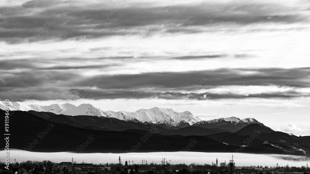 Fototapeta premium Black and white image of the Julian Alps overlooking the Friulian plain covered by a blanket of low clouds. Friuli Venezia Giulia, Italy.
