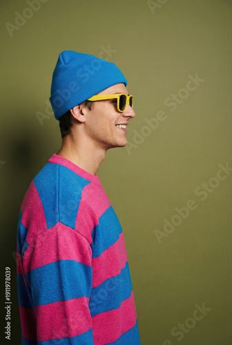 A smiling young man wearing a blue beanie, yellow sunglasses, and a pink and blue striped sweater.