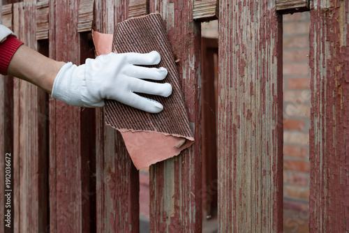 Bild auf Leinwand Person restoring a wooden fence with a sanding block in the late afternoon