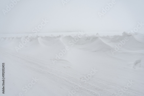 фотографія Wind shaped snow drifts in whiteout winter landscape with icy rural road, extrem