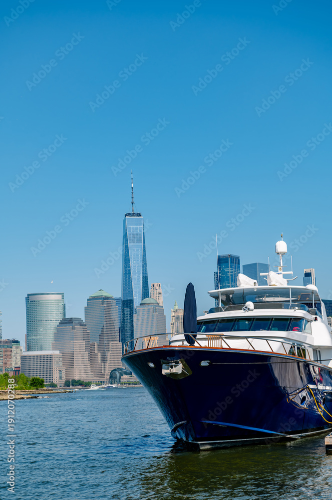 Fototapeta premium Low angle view of a dark blue yacht at a pier with One World Trade Center in the distance.