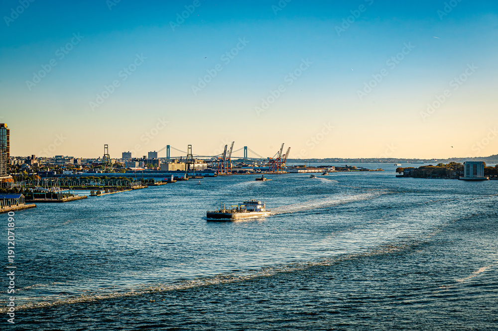 Fototapeta premium Industrial ship moving through water with port cranes and bridge in the background.
