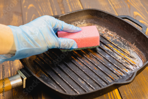 Hand clean rusted cast iron frying pan with sponge. Burnt pot with black bottom. Pan burnt from cooking. Close up.