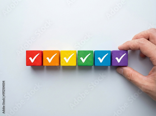 hand places colorful wooden block with checkmark, completing row of similar blocks. It symbolizes task completion, goal achievement, or project success. sense of accomplishment and progress.