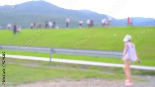 A blurry image of a park with a group of people playing on the grass. Scene is lively and fun, as people are enjoying their time outdoors