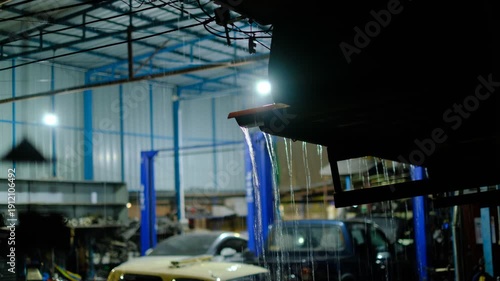 A car is leaking water from its roof. The car is in a garage with other cars. The garage is lit up, but the car is in the dark