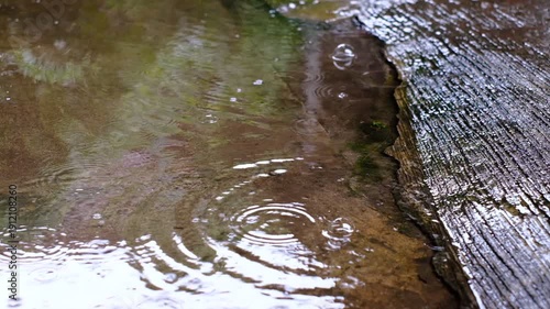 Raindrops on a wooden surface. The rain is falling in a steady rhythm, creating a peaceful atmosphere