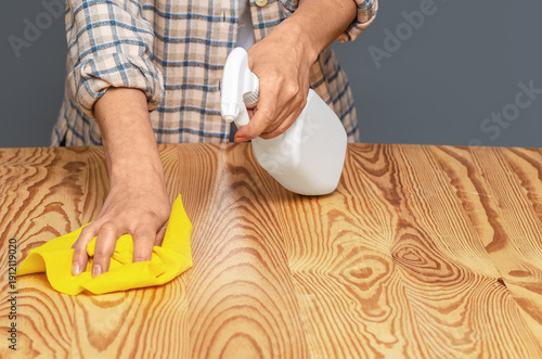 Person in casual clothes wipes wooden surface. Concept of house cleaning, hygiene and surface care.