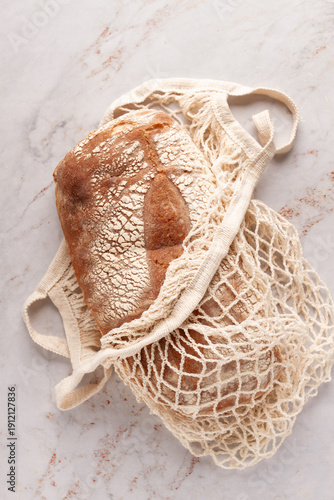 freshly baked rye bread, ciabatta, in a mesh bag, on a marble light table, natural light,