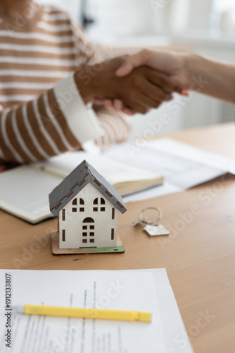 handshake between two people, conclusion of contract for sale of real estate. architectural and design project contract. buying or renting an apartment. miniature model of house stands on table.