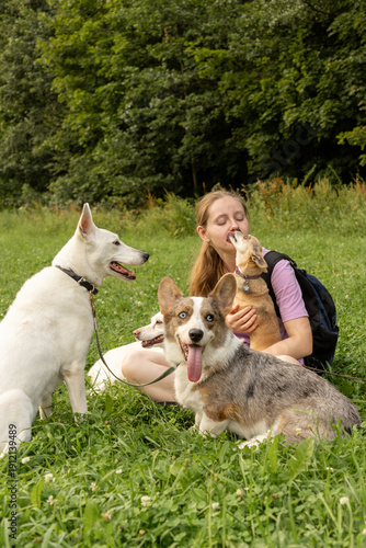 фотографія Professional dog walker young woman with pack of dogs is sitting on green grass and enjoying walk with animals