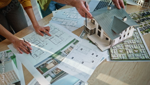 Architects hands pointing blueprints analyzing building model at office closeup.
