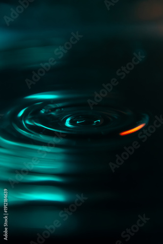 A stunning macro shot of a water drop falling into a liquid surface, creating elegant ripples. High contrast teal and orange colors on a black background. Ideal for creative design and wallpapers.