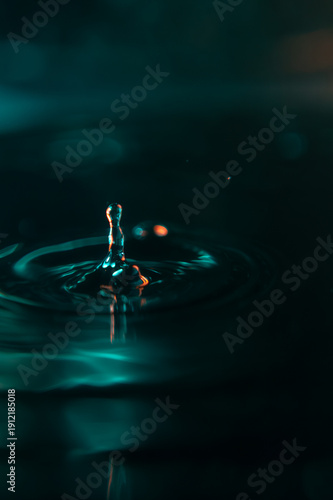 A stunning macro shot of a water drop falling into a liquid surface, creating elegant ripples. High contrast teal and orange colors on a black background. Ideal for creative design and wallpapers.