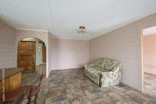 Fotografia A modest living room with patterned sofa, tiled floor, wooden door, arched doorw