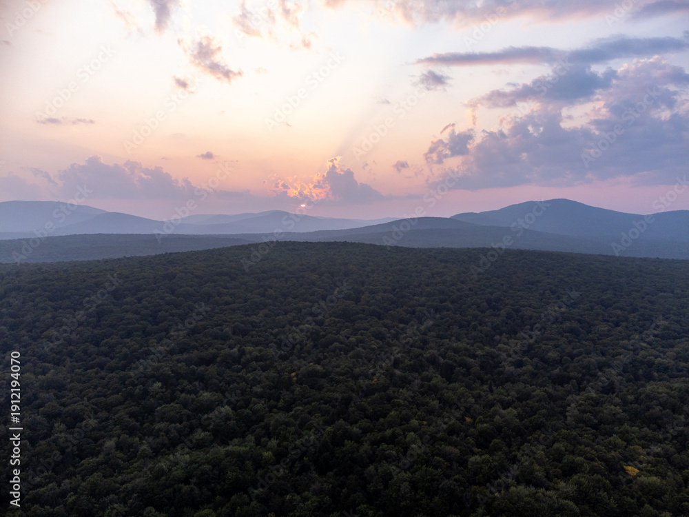 Fototapeta premium Aerial sunset view of rolling green mountain ridges and dense forest in Maidstone, Vermont.