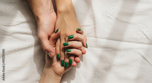 Two hands interlocked on white textile, one with green manicure, representing affection and bond, suitable for relationship or care themes