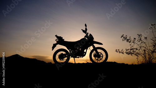 A motorcycle silhouetted against a beautiful sunset sky, exuding a sense of freedom and adventure. The motorcycle is poised on a rugged terrain, hinting at thrilling off-road journeys 