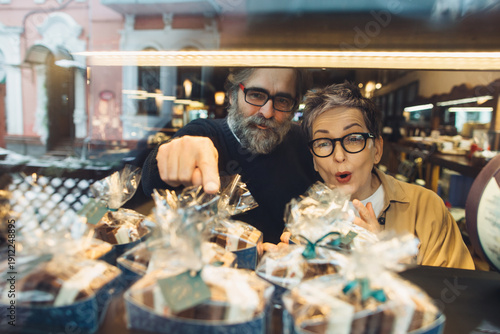 Fotografie Mature couple choosing sweet treats in bakery window