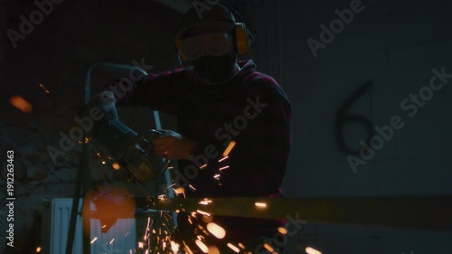 Male industrial or construction worker cuts metal with a angle grinder. Man uses circular saw at garage or workplace. Cutting raw material with flying red sparks at the factory or plant. Slow motion