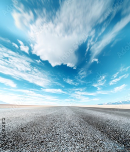 Empty asphalt road stretching into the distance under a vast blue sky with dynamic clouds looking like a journey, travel, freedom, and future concept