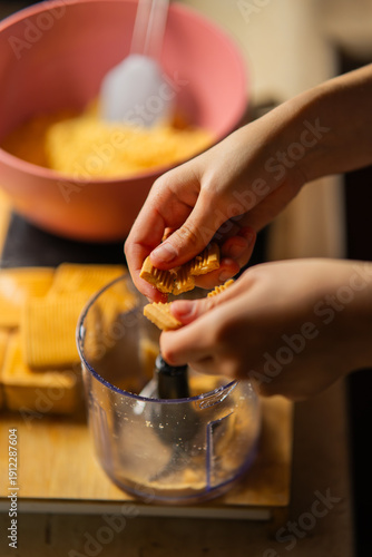 Photos Hands breaking biscuits into a food processor to create crumbs for a dessert base, with a bowl of prepared crumbs in the background, illustrating home baking