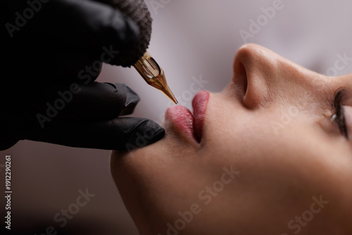 Fotografía closeup of lip tattoo procedure on young female with tattoo machine, beauty cosm