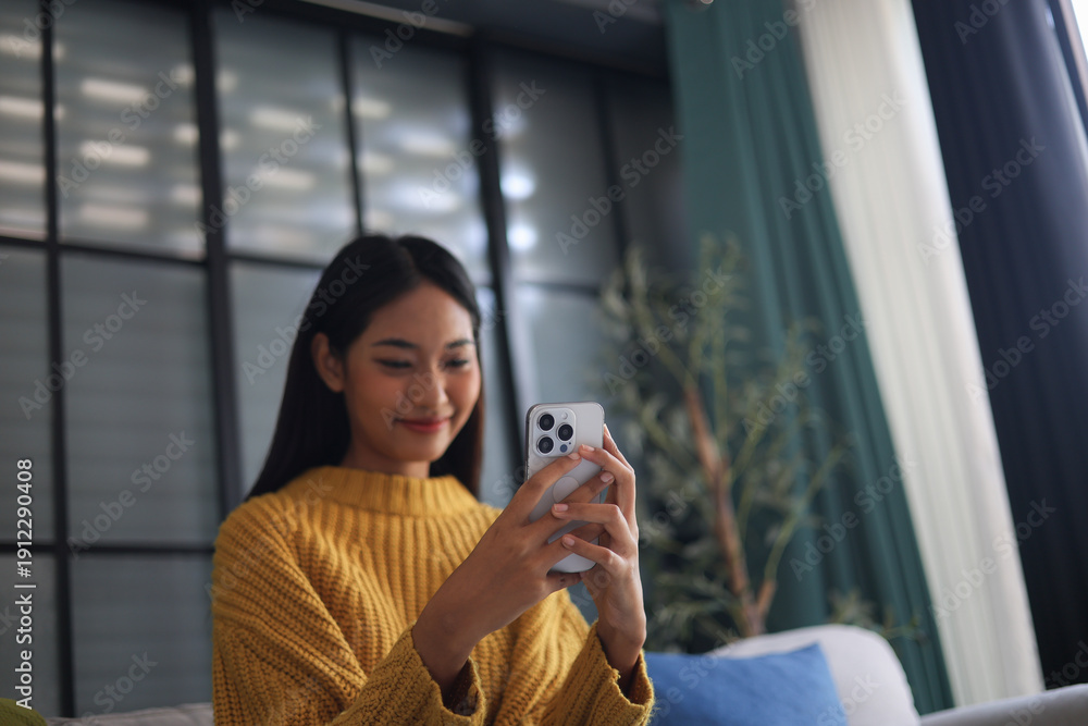 Fototapeta premium Relaxed woman sitting on the couch using phone at her home.