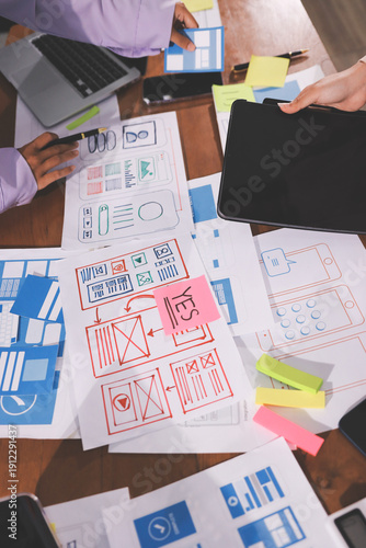 Close up ux developer and ui designer brainstorming about mobile app interface wireframe design on table with customer breif and color code at modern office.Creative digital development agency.