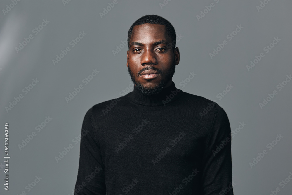 Obraz premium African man portrait with serious expression wearing black turtleneck sweater in creative conceptual visual style on gray background. Studio shot with focused lighting and neutral tone.