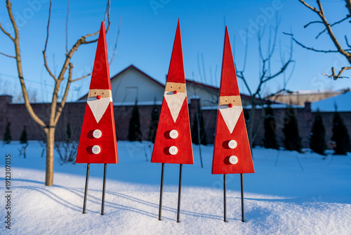 Winter Christmas decorative ornaments: three whimsical gnomes as a symbol of good luck in the new year. Handmade wooden gnomes with red hats against the backdrop of a winter garden, closeup