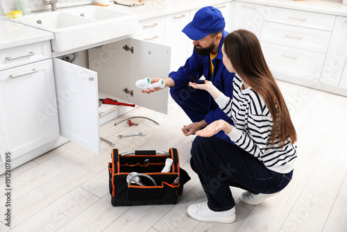 Foto Young woman talking with plumber in kitchen